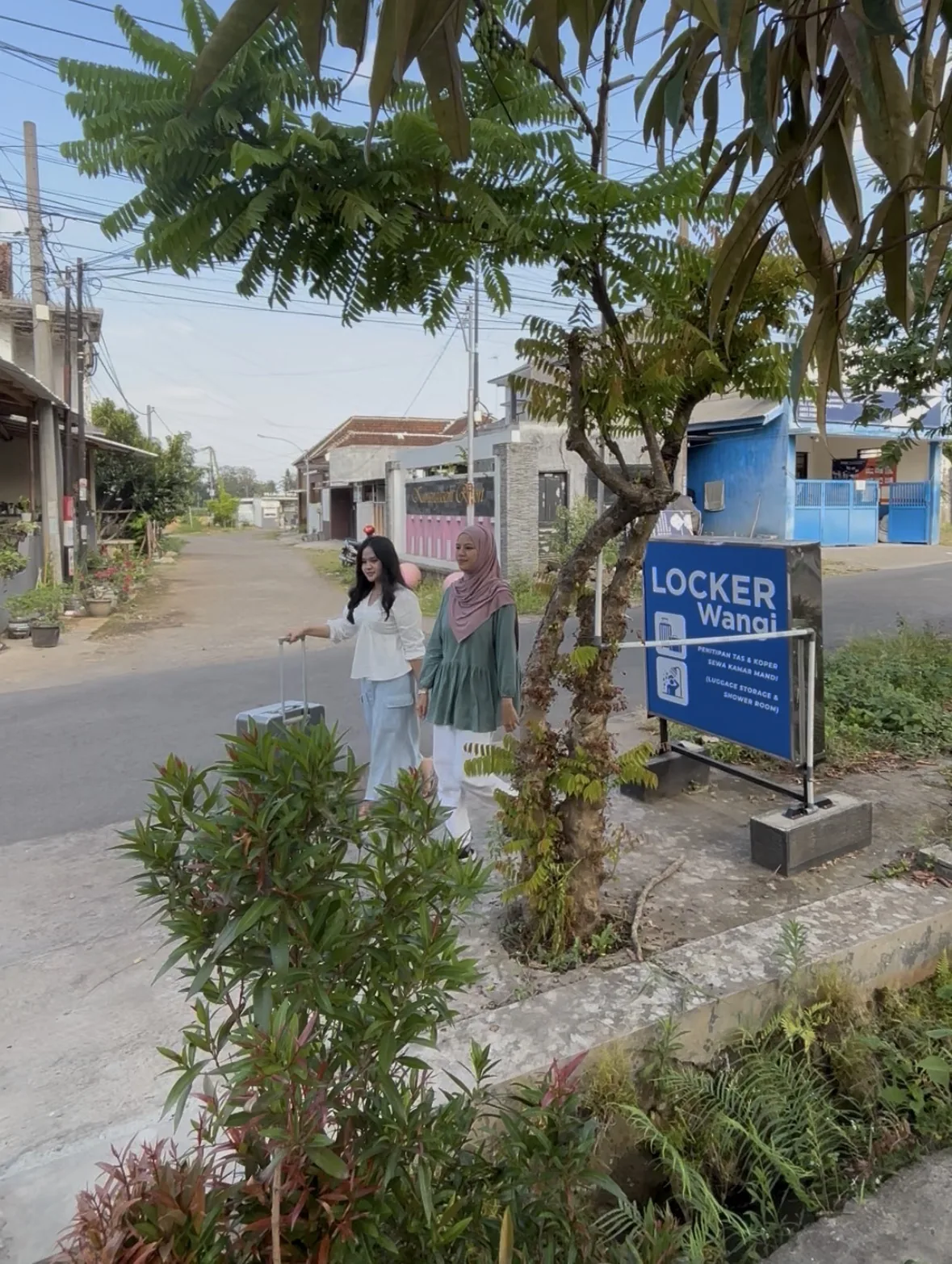 Dua wisatawan membawa koper di dekat papan penunjuk LockerWangi Banyuwangi